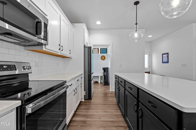 kitchen with pendant lighting, tasteful backsplash, white cabinetry, wood-type flooring, and stainless steel appliances