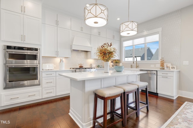 kitchen with premium range hood, appliances with stainless steel finishes, white cabinetry, and hanging light fixtures