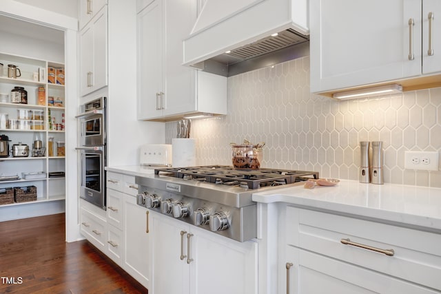 kitchen with premium range hood, decorative backsplash, stainless steel gas cooktop, light stone countertops, and white cabinets