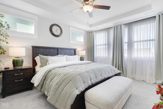 carpeted bedroom with ceiling fan and a raised ceiling