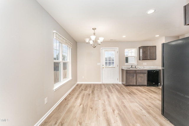 kitchen featuring light wood-type flooring, dark brown cabinetry, black appliances, pendant lighting, and a chandelier