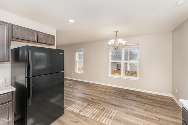 kitchen with black refrigerator, light wood-type flooring, dark brown cabinets, a healthy amount of sunlight, and a chandelier