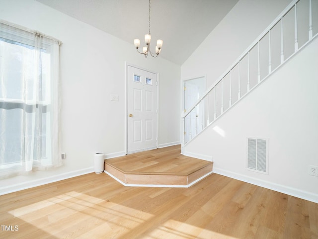 entryway featuring hardwood / wood-style floors, lofted ceiling, and a chandelier