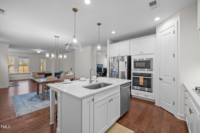 kitchen featuring a kitchen island with sink, appliances with stainless steel finishes, hanging light fixtures, sink, and white cabinetry