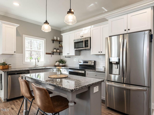 kitchen with white cabinetry, stainless steel appliances, a center island, sink, and dark stone countertops