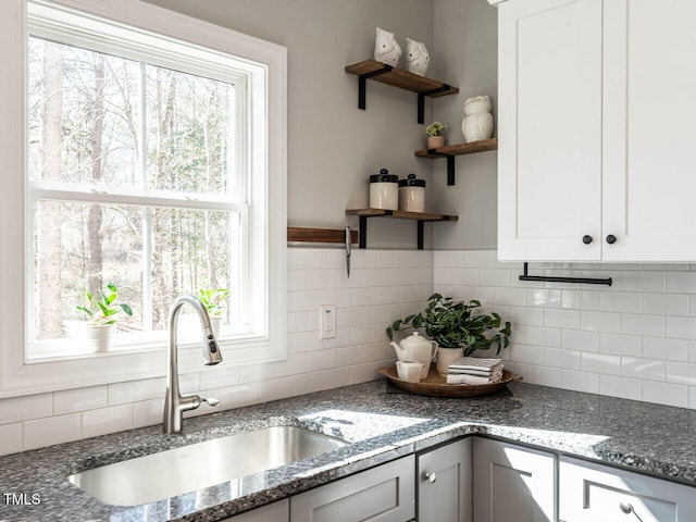 kitchen featuring white cabinets, dark stone countertops, a wealth of natural light, and sink