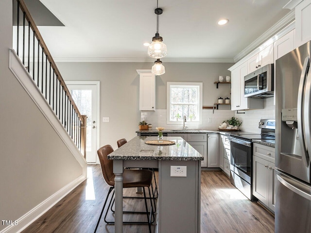 kitchen with stainless steel appliances, hanging light fixtures, a kitchen island, white cabinets, and a breakfast bar area