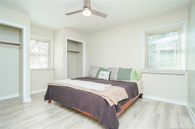 bedroom with multiple closets, ceiling fan, multiple windows, and light wood-type flooring