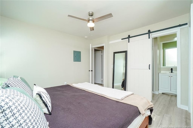 bedroom with electric panel, ensuite bath, ceiling fan, a barn door, and light hardwood / wood-style floors