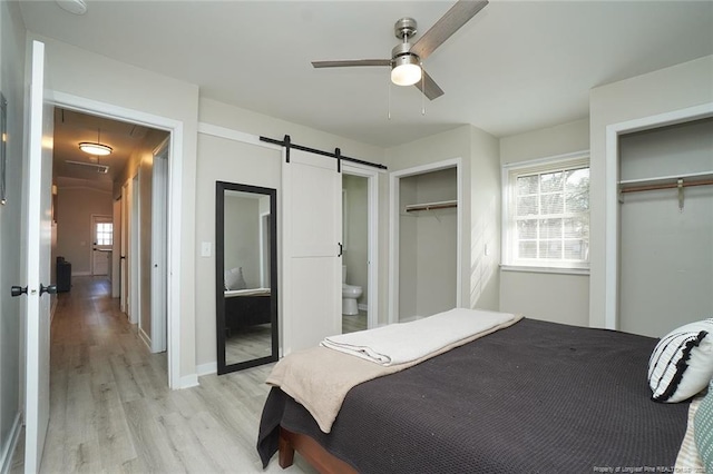 bedroom featuring ceiling fan, a barn door, ensuite bathroom, and two closets