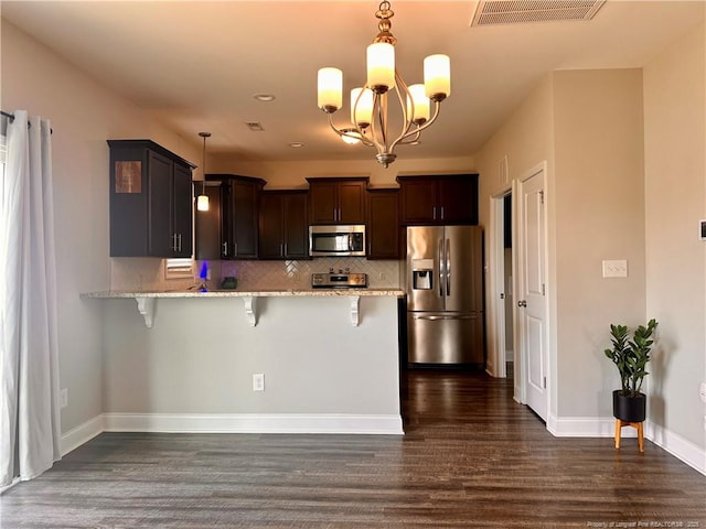 kitchen with kitchen peninsula, appliances with stainless steel finishes, a kitchen breakfast bar, tasteful backsplash, and pendant lighting