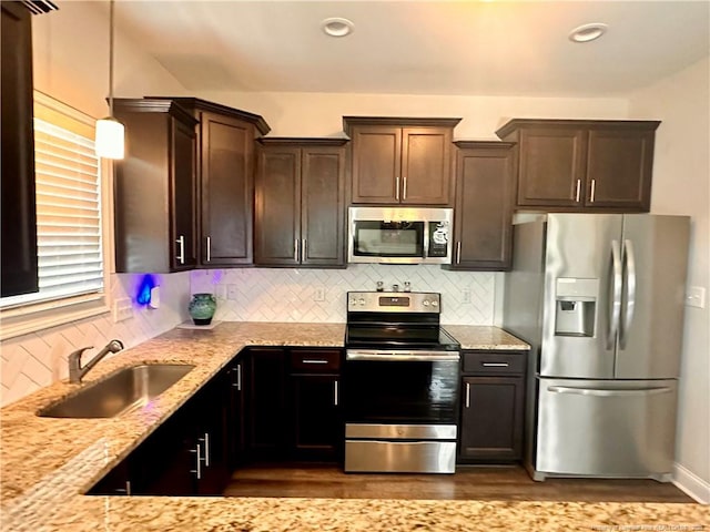 kitchen with light stone countertops, sink, stainless steel appliances, tasteful backsplash, and decorative light fixtures