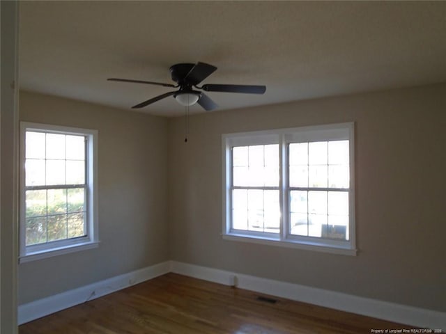 empty room featuring plenty of natural light, ceiling fan, and dark hardwood / wood-style flooring