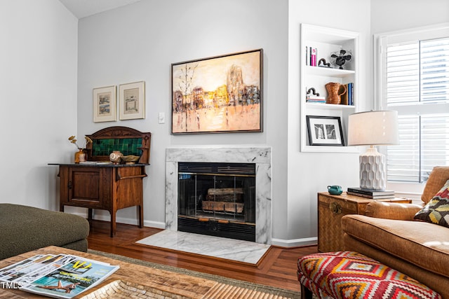 living room with built in features, a high end fireplace, and wood-type flooring