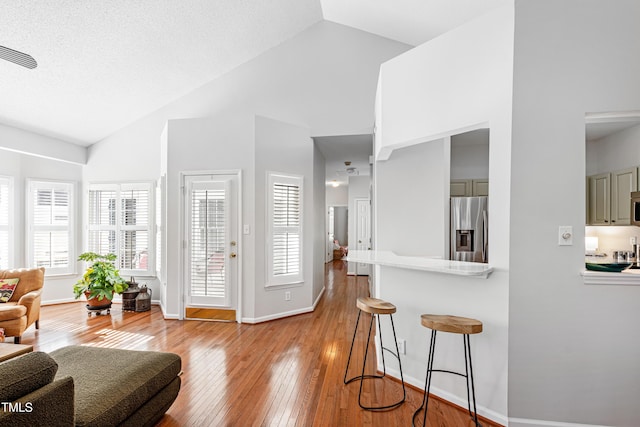 living room with vaulted ceiling, a textured ceiling, and light hardwood / wood-style floors