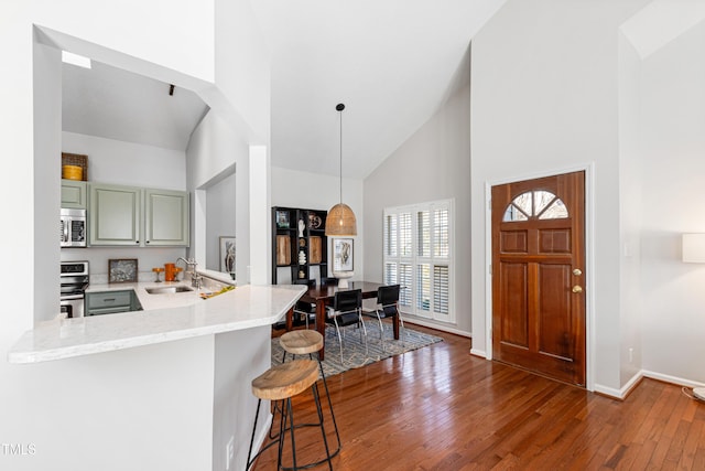 kitchen featuring sink, decorative light fixtures, kitchen peninsula, a breakfast bar area, and high vaulted ceiling