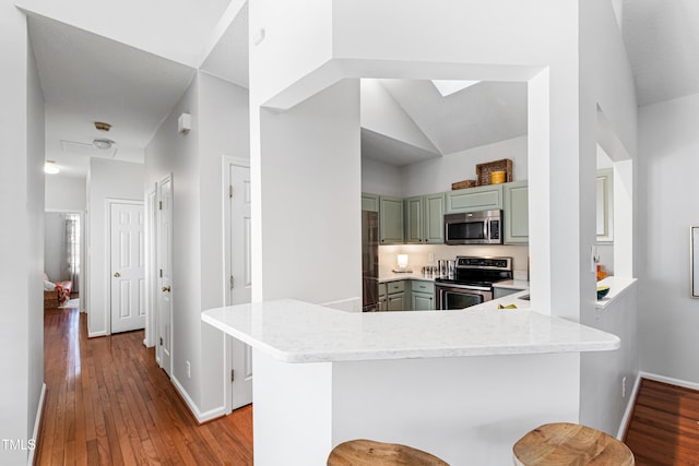 kitchen with kitchen peninsula, vaulted ceiling, stainless steel appliances, a breakfast bar, and light wood-type flooring