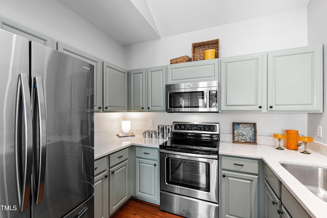 kitchen featuring dark wood-type flooring, a textured ceiling, gray cabinets, appliances with stainless steel finishes, and sink