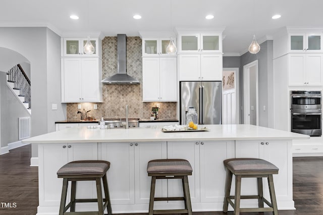 kitchen with stainless steel appliances, a kitchen island with sink, crown molding, and wall chimney exhaust hood