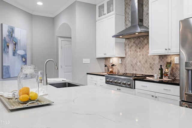 kitchen featuring white cabinets, wall chimney exhaust hood, ornamental molding, and appliances with stainless steel finishes