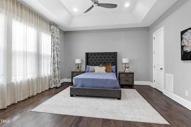 bedroom with ceiling fan, dark hardwood / wood-style flooring, and a tray ceiling