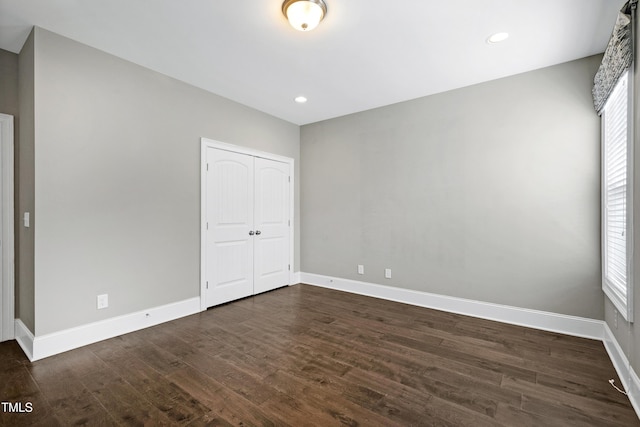 unfurnished bedroom with multiple windows, a closet, and dark hardwood / wood-style floors