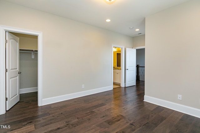 unfurnished bedroom featuring a walk in closet, a closet, ensuite bath, and dark hardwood / wood-style floors