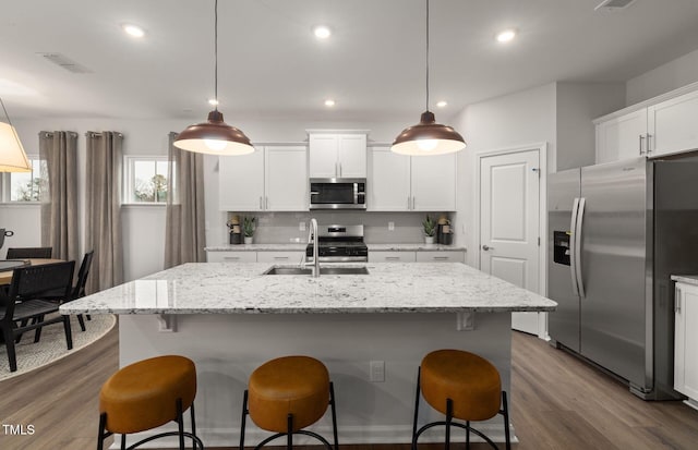 kitchen with stainless steel appliances, sink, white cabinets, pendant lighting, and a kitchen island with sink