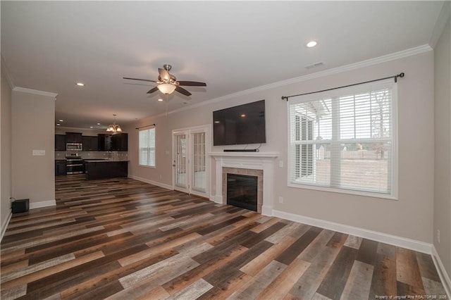 unfurnished living room featuring a tiled fireplace, crown molding, dark hardwood / wood-style floors, and ceiling fan with notable chandelier