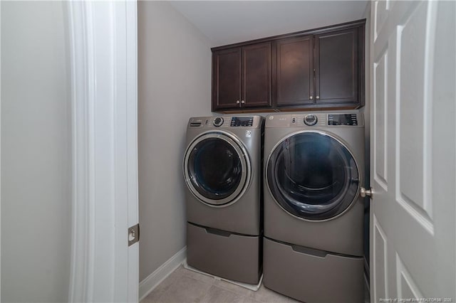 clothes washing area with washer and clothes dryer, cabinets, and light tile patterned floors