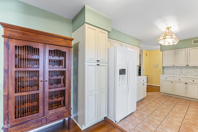 kitchen featuring tasteful backsplash, white cabinetry, white refrigerator with ice dispenser, and pendant lighting