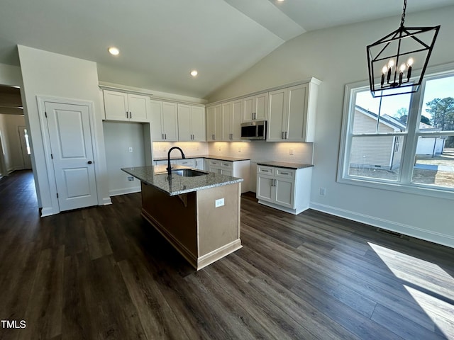 kitchen featuring an island with sink, stainless steel microwave, white cabinets, and a sink