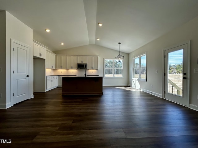 kitchen with white cabinets, stainless steel microwave, open floor plan, hanging light fixtures, and a kitchen island with sink