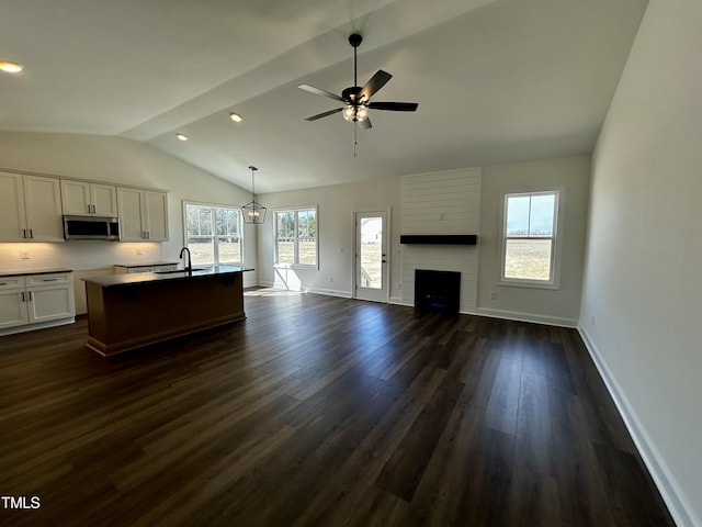 kitchen with white cabinets, an island with sink, dark wood-style floors, stainless steel microwave, and open floor plan