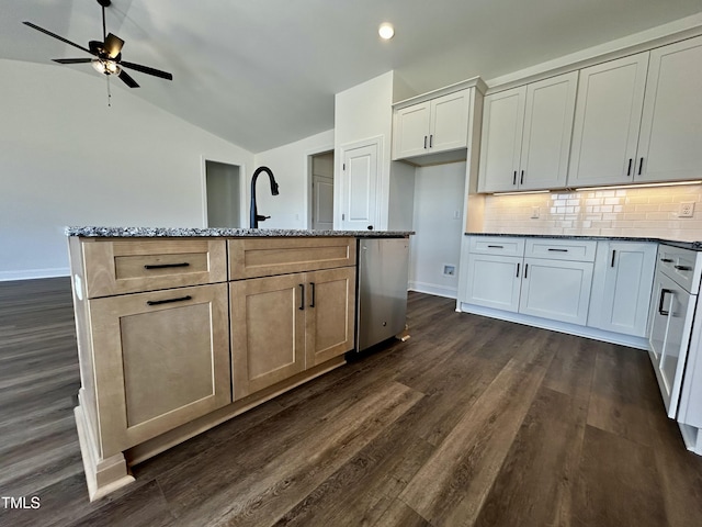 kitchen featuring vaulted ceiling, light stone counters, dark wood-style flooring, and a center island with sink