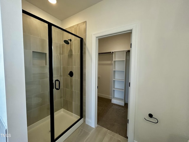 bathroom featuring a shower stall, a spacious closet, and baseboards