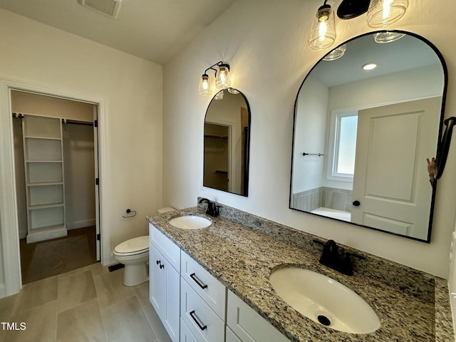 bathroom with a walk in closet, visible vents, a sink, and double vanity