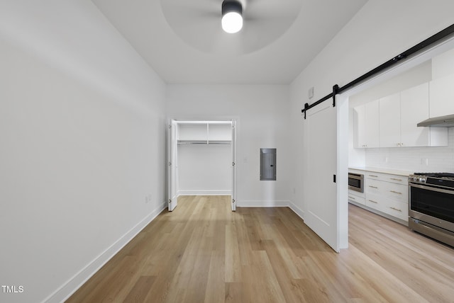 kitchen featuring stainless steel gas stove, white cabinetry, backsplash, a barn door, and light wood-type flooring