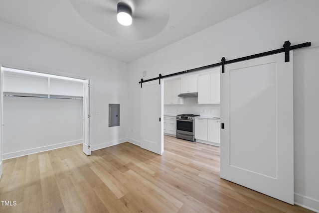 kitchen featuring ceiling fan, white cabinetry, electric panel, gas range, and a barn door