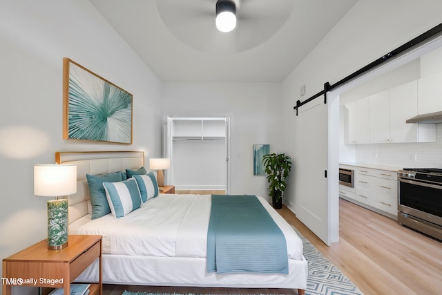 bedroom with light hardwood / wood-style flooring, a spacious closet, ceiling fan, a barn door, and a closet