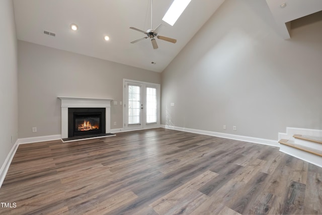 unfurnished living room with wood-type flooring, a skylight, ceiling fan, french doors, and high vaulted ceiling