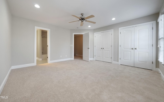 unfurnished bedroom with ensuite bathroom, two closets, ceiling fan, and light carpet