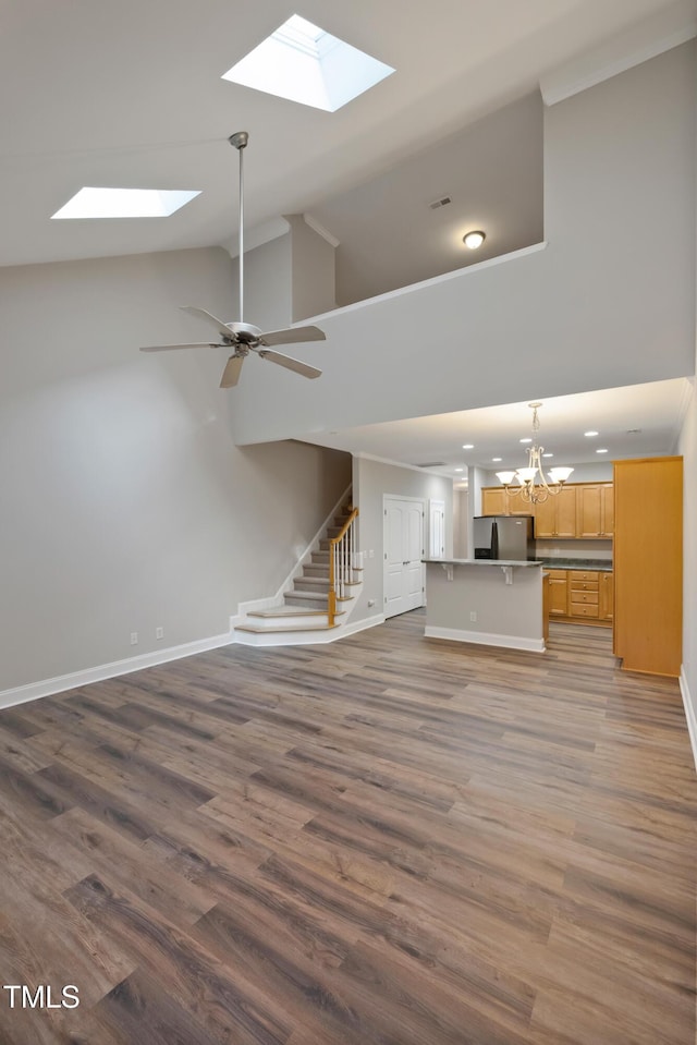 unfurnished living room featuring high vaulted ceiling, ceiling fan with notable chandelier, and wood-type flooring