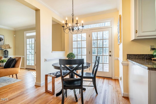 dining area with a notable chandelier, light wood-type flooring, a wealth of natural light, and crown molding