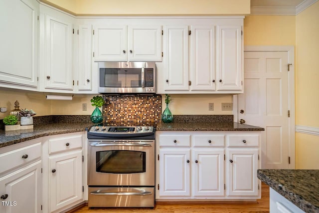 kitchen featuring appliances with stainless steel finishes, white cabinetry, dark stone counters, and ornamental molding