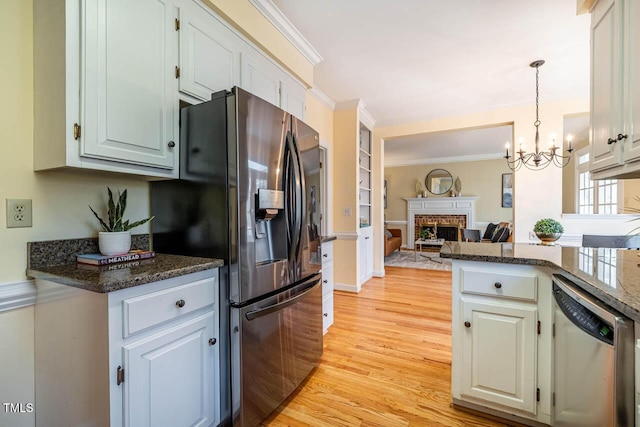 kitchen with white cabinetry, stainless steel appliances, a fireplace, light hardwood / wood-style flooring, and an inviting chandelier