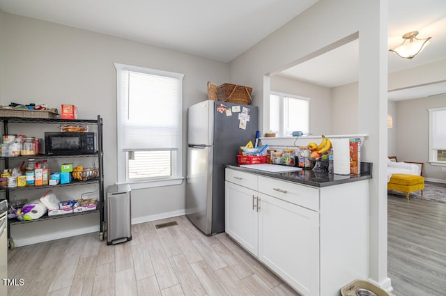 kitchen with white cabinets, light wood-type flooring, and stainless steel refrigerator