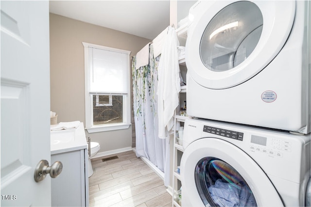 laundry area with light hardwood / wood-style flooring and stacked washing maching and dryer