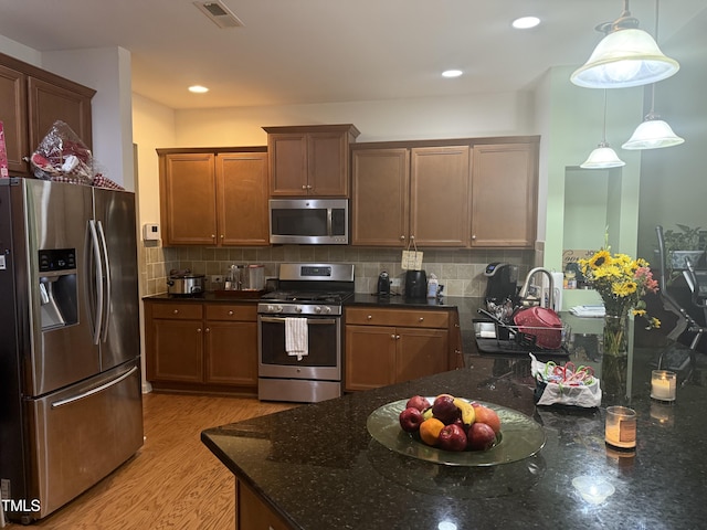 kitchen with dark stone countertops, decorative backsplash, hanging light fixtures, stainless steel appliances, and light wood-type flooring