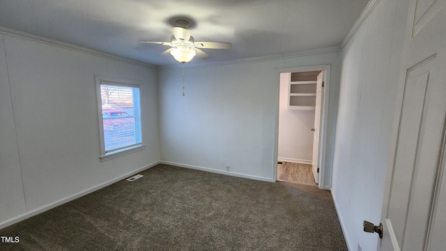 unfurnished bedroom featuring dark colored carpet, a spacious closet, ceiling fan, and ornamental molding